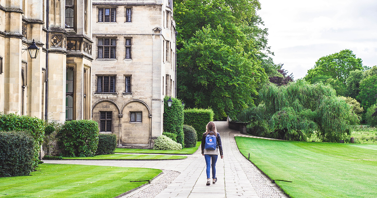 woman walking alone on college campus, lots of trees