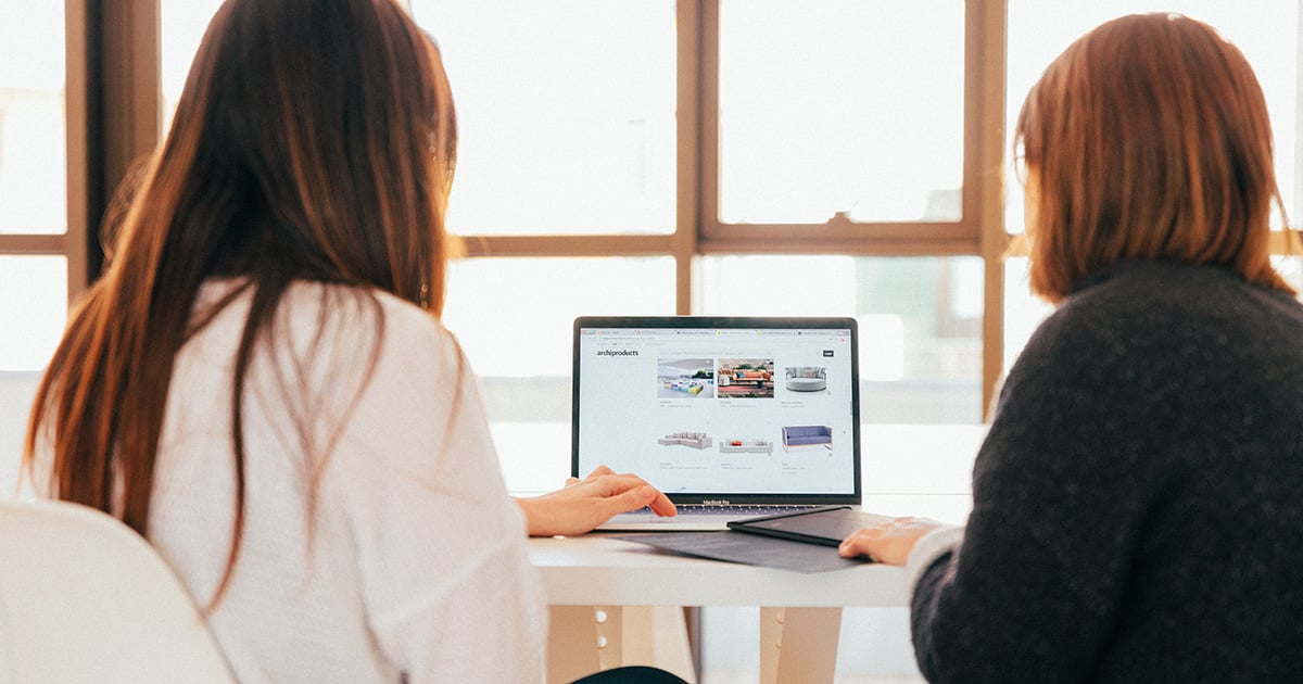 two women's backs face the camera while they look at a laptop screen, showing photos that need alt text