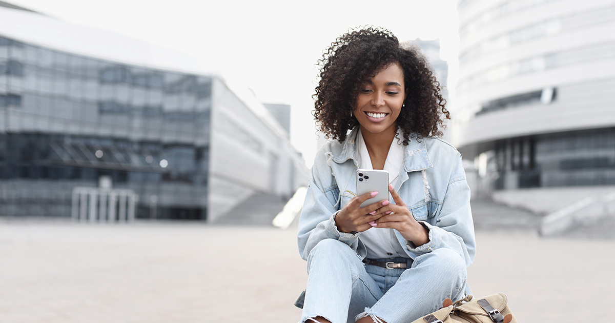 Black female student wearing light denim outfit smiles at her smartphone